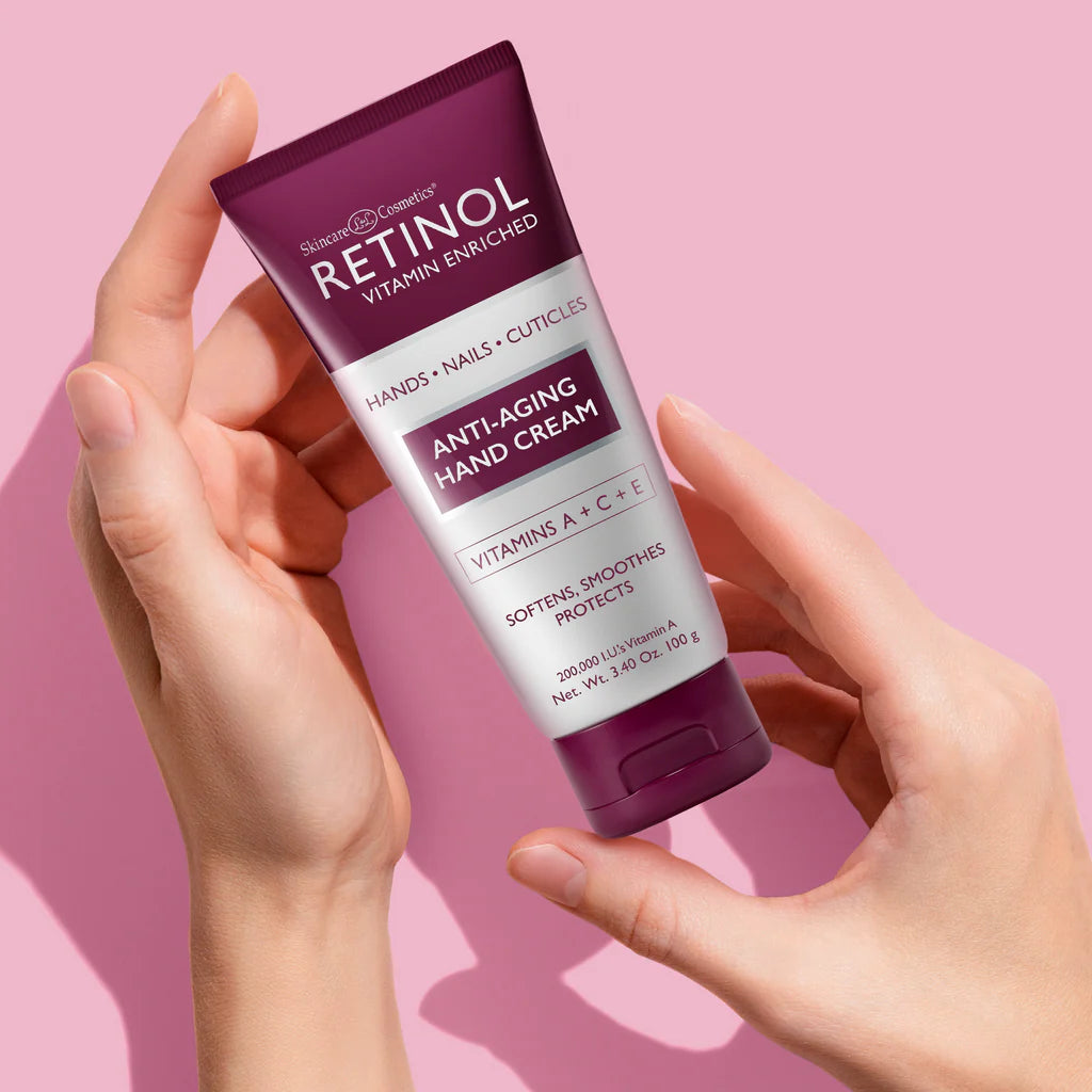 Hand holding a tube of Retinol anti-aging hand cream against a pink background