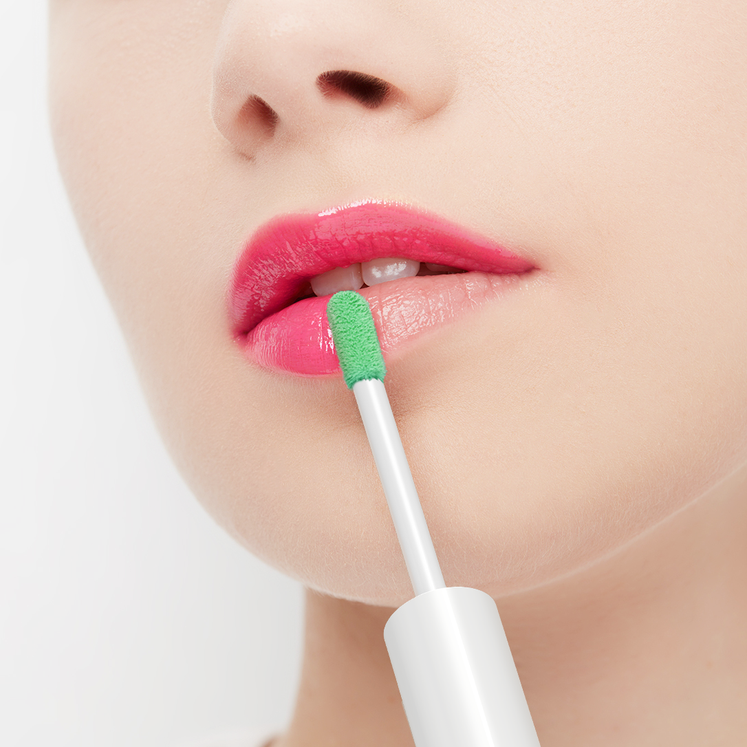 Lipstick with a green cap being applied to lips on a white background